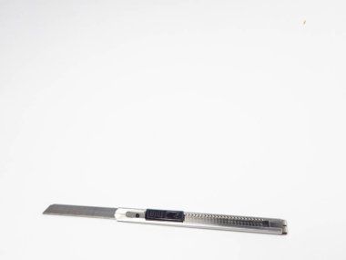 Beyaz bir yüzey üzerinde duran gümüş bir alet bıçağının yakın plan çekimi. Görüntü, aletin keskin bıçağını ve metalik detaylarını vurgular. Hassasiyet, kesim, DIY projeleri, el işi, ofis malzemeleri veya Shar gibi kavramları resmetmek için idealdir.