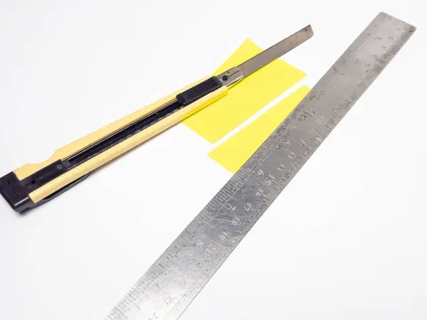 Tepeden çekimde bir bıçak, bir metal cetvel ve beyaz arka planda iki şerit sarılı kağıt var. Resim, el sanatları, DIY projeleri veya ofis gereçleri için mükemmel olan kesim veya ölçüm araçlarını yakalar. Şey... 