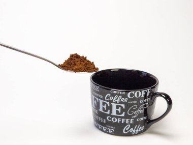 Yakın çekim bir kaşık tasvir eder hazır kahve tanecikleri bir tepecik tutan, siyah bir kahve fincanı üzerinde duran. Kupa çeşitli yazı tiplerinde 