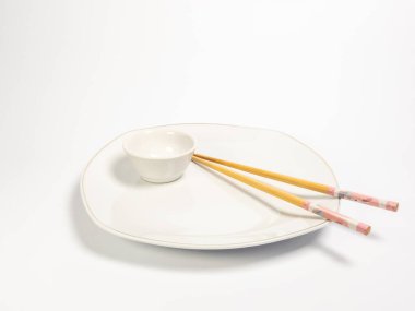 Asyalı yemek düzenini gösteren minimalist bir natüralist. Sergide beyaz bir oval tabak, küçük bir eşleşen kase ve tabakta dinlenen bir çift çubuk yer alıyor. Ayar temiz ve basit, parlak beyaz arkaplanlı, altı çizili