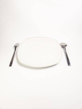 Beyaz bir plaka, bir çatal ve beyaz arka planda bir kaşık gösteren minimalist bir natüralist. Kompozisyon temiz ve basit. Boş tabağı vurguluyor. Bekleyen bir yemek ya da boşluk kavramını çağrıştırıyor. Işıklandırma yumuşak ve her...