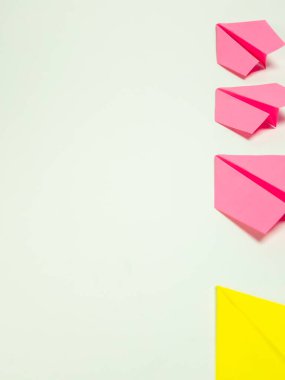 Pembe ve sarı renkli katlanmış kağıt uçaklardan oluşan görsel olarak çekici bir görüntü. Uçaklar temiz, beyaz bir zemine göre ayarlandı. Görüntü iyi aydınlatılmış, canlı ve modern bir estetik yaratıyor. Tasarımlar için mükemmel.