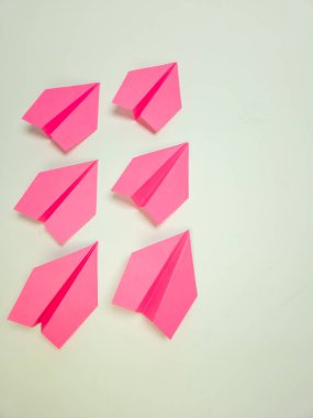 Bu resim düz beyaz bir zemin üzerinde düzenlenmiş altı canlı pembe kağıt uçak içeriyor. Uçaklar eşit aralıklı ve açılı, görsel olarak çekici bir bileşim oluşturuyor. Işıklandırma yumuşak ve hatta parlak pembe rengi vurguluyor ve...