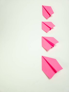 Beyaz arka planda dikey olarak dizilmiş dört pembe kağıttan uçağın yukarıdan aşağı görüntüsü. Uçaklar özenle hazırlanmış, origami tekniğini vurguluyorlar. Kompozisyon temiz ve minimalist. Basitliği ve oyunculuğu vurguluyor.