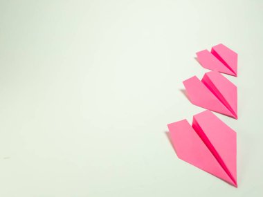 Soluk yeşil arka planda çapraz dizilmiş üç pembe kağıt uçak. Görüntü, kağıt uçakların basitliğini ve temiz çizgilerini vurgulayan iyi ışıklandırılmış ve minimalistik. Uçaklar odak noktası, geniş negatif alan yaratıyor.