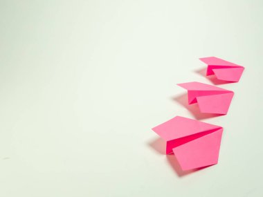 Üç pembe kağıt uçak, soluk, tarafsız bir arkaplana karşı köşegen olarak dizilmiştir. Görüntü ışıl ışıl parlıyor ve uçakların altında yumuşak gölgeler var. Üç boyutlu formlarını vurguluyorlar. Kompozisyon, trave temalarını öneriyor.