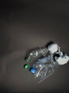 Bu resim, arka planda sıralanmış şişe, bardak ve ambalaj da dahil olmak üzere atılmış plastik atıklardan oluşan bir koleksiyonu gösteriyor. Belge, plastik kirliliğinin artan çevresel kaygılarını ve etkilerini vurguluyor. Kompozisyon henüz basit.
