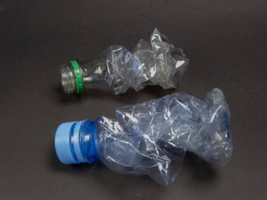 Birinde yeşil kapaklı, diğerinde mavi kapaklı iki buruşuk plastik şişe koyu gri arka plana yerleştiriliyor. Şişeler ciddi şekilde deforme olmuş. Yani ya atılmış ya da ezilmiş. Bu resim r kavramlarını göstermek için idealdir