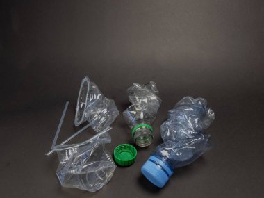 Birkaç kırık plastik şişe, kapak ve siyah arka planda bir pipet yakın çekim. Görüntü, çevre sorunlarını vurgulayarak, plastik atık ve kirliliğin doğrudan bir tasviri. Kompozisyon dokuyu ve şeffaflığı vurgular