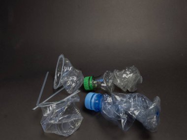 Bir fotoğraf, atılmış plastik şişeleri ve karanlık bir yüzeyde buruşmuş pipetleri gösteriyor. Görüntü, plastik atık ve çevre kirliliği sorununu vurguluyor. Bileşim, plastiğin dokusunu ve şeffaflığını vurgular ve oluşturur.