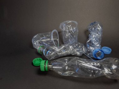 Buruşuk, berrak plastik şişeler ve koyu, katı bir yüzeye saçılmış bir fincan. Görüntü, plastik atık sorununu ve çevre üzerindeki etkisini vurguluyor. Kompozisyon, iyi ışıklandırmalı basit, doğrudan bir sunum içeriyor