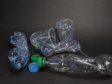 Karanlık bir yüzeye saçılmış plastik şişe ve fincanları gösteren bir resim. Kompozisyon, tek kullanımlık plastik maddelerin atık ve çevresel etkilerini vurguluyor. Fotoğraf plastiğin dokusunu ve şeffaflığını vurgular.