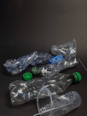 Atık ve kirlilik sorununu vurgulayarak, karanlık bir zemine saçılmış buruşmuş plastik şişeler ve fincanlar koleksiyonu. Görüntü plastik atıkların görsel etkisini vurguluyor, çeşitli şekilleri, boyutları ve renkleri gösteriyor. Kompozisyon... 