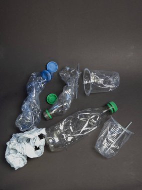 Plastik kirlilik ve atık sorununu vurgulayan ezilmiş plastik şişeler, kapaklar ve kamışlı bir fincan koyu gri arka plana saçılmıştır. Bu resim çevresel kaygıları, geri dönüşümü ve i 'yi göstermek için uygundur.