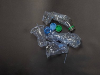 Yukarıdan çekilen bir karede, arka planda atılmış plastik atıklar sergileniyor. Görüntüde çeşitli buruşmuş plastik şişeler, bardaklar, şişe kapakları ve çevresel kirlilik sorununu görsel olarak temsil eden bir pipet yer alıyor.