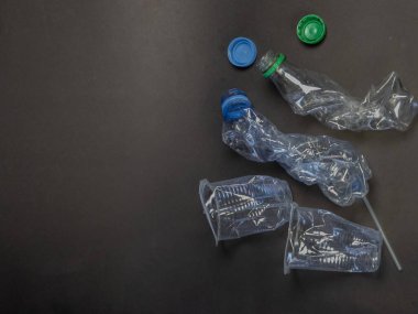 Bu yukarıdan çekilen görüntüler plastik şişeleri ve kapakları koyu gri bir yüzeye serpiştirmiş. Görüntü, plastik atık ve çevresel kaygıları vurguluyor. Kompozisyon basit, atılanın dokularını ve şekillerini vurguluyor.