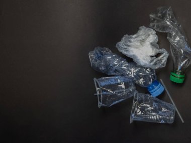 Kırışmış plastik şişeler ve arka plana saçılmış plastik bardaklardan oluşan bir koleksiyon. Görüntü, plastik tüketiminin etkisini gösteren geri dönüşüm ve atık yönetimi kavramını vurguluyor. Kompozisyon dokuyu vurguluyor.