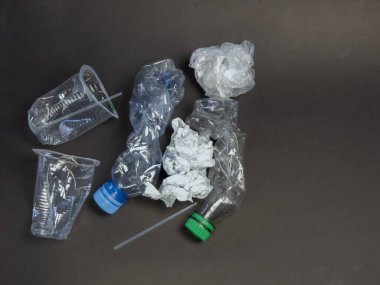 Tepeden çekimde plastik atıklar görülüyor. Koyu gri bir yüzeyde şişeler, bardaklar ve buruşuk plastikler de dahil. Görüntü, plastik kirliliği ve geri dönüşüm ihtiyacını vurguluyor. Bileşimi basit, plastik atık...