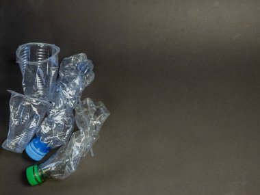 Karanlık bir yüzeyde buruşmuş plastik şişeler ve bardaklar. Görüntü, plastik atık sorununu ve bunun çevresel etkilerini vurguluyor. Parçaların dokuları ve şekillerine odaklanarak kompozisyon basittir. Karanlık...