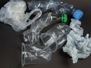 Bu resim, koyu bir arkaplanda sıralanmış şişe, bardak ve plastik poşetler de dahil olmak üzere atılmış plastik eşyalar koleksiyonunu tasvir eder. Kompozisyon, plastik atıkların yaygınlığını ve bunun çevre üzerindeki etkisini vurguluyor. Resim bir ileti iletir