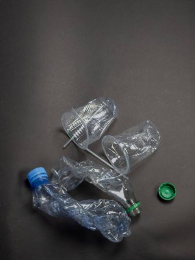 Şişeler ve fincanlar da dahil olmak üzere atılan plastik atıkların karanlık bir arkaplana karşı tepetaklak çekilmesi. Görüntü, plastik kirliliğinin çevresel etkisini vurguluyor. Bileşim, atıkların hacmini ve sorumlu imha ihtiyacını vurgular. 