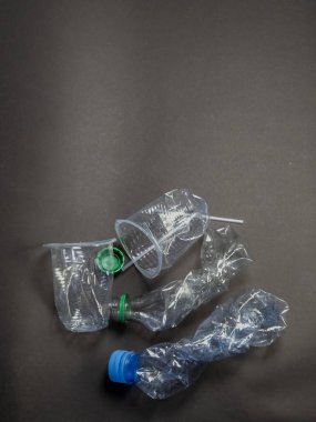 Bu üstten çekimde koyu arkaplanda ezilmiş plastik bardaklar ve şişeler var. Görüntü, plastik atık sorununu ve çevre üzerindeki etkisini vurguluyor. Atık, kirlilik ve geri dönüşüm ihtiyacını iletir.. 