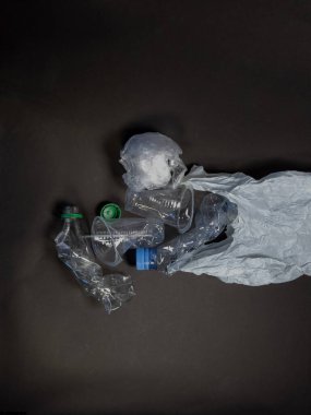 Şişeler, fincanlar ve plastik torba da dahil olmak üzere buruşuk plastik atıkların koyu gri veya siyah bir zemin ile genel görüntüsü. Görüntü, çevre kirliliği sorununu ve geri dönüşüm ve atık yönetimi ihtiyacını vurguluyor. Fotoğraf...