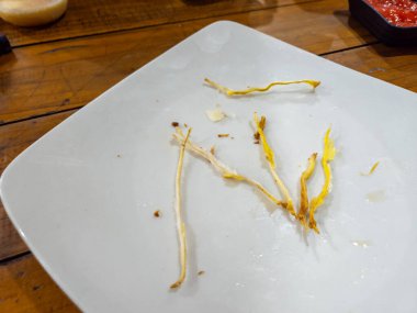 Tahta bir masada yemek yedikten sonra beyaz tabakta kalan yemek.