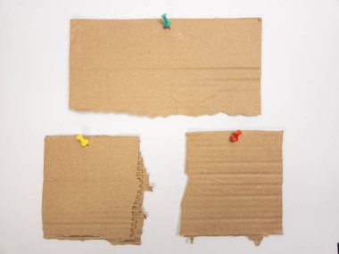 Bir natürmort beyaz arka planda renkli raptiyeli üç parça yırtık karton gösteriyor. Karton parçaların farklı şekilleri ve yırtık kenarları var. İtme iğneleri yeşil, sarı ve kırmızı. Kompozisyon basit ve minimalist.