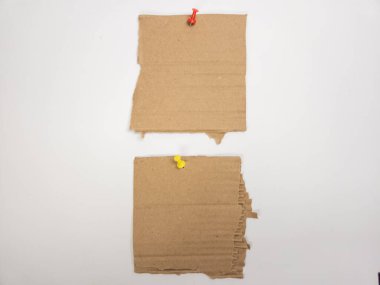 Yüksek açılı bir çekimde düz beyaz bir arkaplanda iki adet yırtık karton parçası görülüyor. Üstteki parça kırmızı bir iple tutturulurken, alttaki ise sarı bir iple tutturuluyor. Kartonun pürüzlü, desenli bir yüzeyi var ve bir simülasyon oluşturuyor.