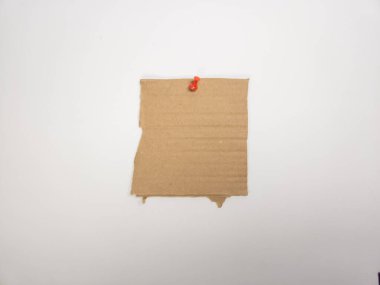 Kare bir kahverengi karton parçası kırmızı raptiyeli beyaz bir arka plana tutturulur. Kartonda yırtık bir kenar var ve biraz desenli. Görüntü, kahverengi ve beyaz arasındaki kontrast üzerine odaklanmış basit, minimalist bir kompozisyon. Şey...