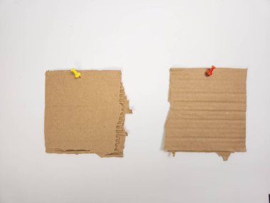 İki kare kahverengi karton parçası sarı ve kırmızı raptiyeli beyaz bir yüzeye tutturulur. Karton parçaların kenarları pürüzlü, yırtık, desenli bir görünüm yaratıyor. Kompozisyon basit ve minimalist, tasarım veya kavramsal halkla ilişkiler için uygundur.