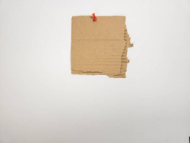 Kırık bir karton parçası beyaz bir yüzeye kırmızı bir iğneyle tutturulur. Kartonun dokusuna ve kompozisyonun basitliğine odaklanıyor. Görüntü iyi aydınlatılmış, temiz ve minimalist bir estetik oluşturuyor. Tarafsız torba.