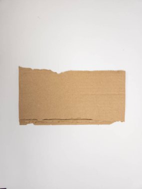 Dörtgen şeklinde yırtık bir kahverengi karton parçası düz beyaz bir arka planda yatıyor. Kartonun üstü ve altı pürüzlü, düz olmayan bir kenarı var. Yırtıldığını ya da kesildiğini gösteriyor. Resim, kartondaki desen ve rengi vurguluyor ve basit bir şekil oluşturuyor.
