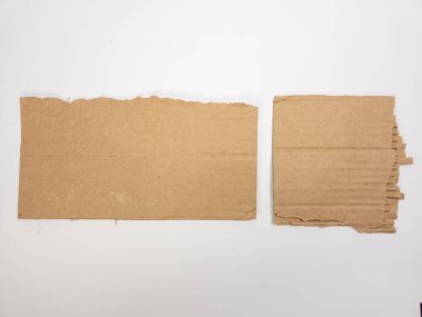 Bu, düz beyaz arka planda iki parça yırtık kahverengi kartondan oluşan bir stüdyo çekimi. Karton parçaların pürüzlü, pürüzlü kenarları var. Dokusunu ve kumaşın yapısını gösteriyor. Çekim yüksek açılı bir perspektiften yapılıyor.