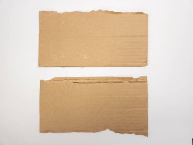 Beyaz bir yüzey üzerinde iki parça yırtık kahverengi karton. Karton parçaların pürüzlü, pürüzlü kenarları var. Yırtılmış ya da yırtılmış olduklarını gösteriyor. Görüntü temiz ve basit, kartondaki doku ve tonlara odaklı. T
