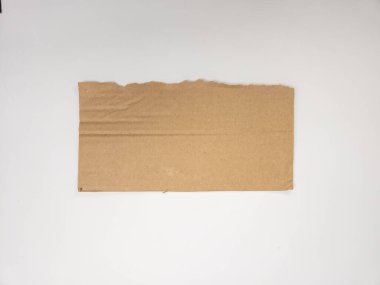 Yırtık kenarlı, temiz beyaz bir arka planda izole edilmiş dikdörtgen bir kahverengi karton parçasının yakın çekim çekimi. Kartonda görünür kıvrımlar ve biraz pürüzlü doku var. Bu da bir kargo kutusu ya da ambalajdan geldiğini gösteriyor. Ben...