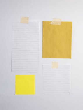 Yakın plan çekimde bir kağıt para koleksiyonu ve yapışkan bir not sergileniyor. Hepsi de temiz beyaz bir arkaplana bantlanmış. Kompozisyonda çizgi kağıt, sarı desenli bir not ve kare sarı yapışkan bir kağıt da dahil olmak üzere çeşitli şekil ve renkler yer alıyor. 