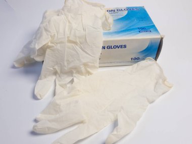 Bir kutu tıbbi lateks eldiven ve beyaz bir yüzey üzerinde iki ayrı eldiven. Eldivenlerin rengi soluk ve kullanılmamış görünüyor. Kutu 100 parça ve tek kullanımlık olduğunu gösteriyor. Görüntü iyi aydınlatılmış, gl 'nin dokusunu vurguluyor.