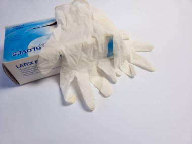 Yakından çekilmiş bir fotoğrafta, beyaz bir yüzeyde duran bir kutu lateks eldiven ve dökülen birkaç eldiven sergileniyor. Görüntü, tıbbi eldivenlerin dokusunu ve detaylarını vurguluyor ve bunlar genellikle sağlık ortamlarında korunmak için kullanılıyor. - Evet.