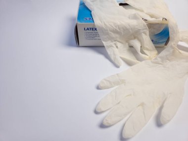 Bu resim beyaz bir yüzeye dağılmış birkaç eldivenli bir kutu lateks eldiven içeriyor. Önemli olan eldivenler, dokuları ve kutunun etiketleri. Kompozisyon temiz ve basit, tıbbi, güvenli ya da hijyen için uygun.