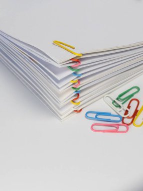 Yakın plan çekimde, çeşitli renkli ataçlarla bir araya getirilmiş beyaz kağıt yığınları sergileniyor. Beyaz yüzeye farklı renklerde birkaç tane ataç serpiştirildi. Kompozisyon temiz ve düzenli bir görsel yaratıyor.