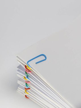 Çeşitli renkli ataçlarla tutturulmuş beyaz kağıt çarşafların yakın plan çekimi. Ataşları mavi, kırmızı, sarı, yeşil ve pembedir, beyaz kağıda bir renk katar. Görüntü temiz, minimalist bir estetiğe sahip.