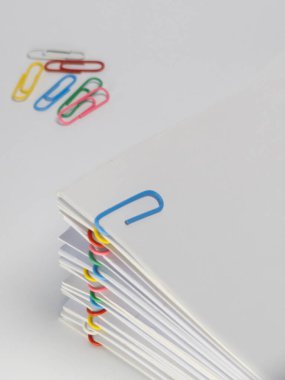 Yakın plan çekimde renkli ataçlarla tutturulmuş beyaz bir kağıt yığını yer alıyor. Kağıtlar mavi, yeşil, pembe, sarı ve kırmızı olmak üzere çeşitli renklerde düzenlenmiştir. Resim düz beyaz bir arkaplan karşısında ayarlanır, bir cl sağlar