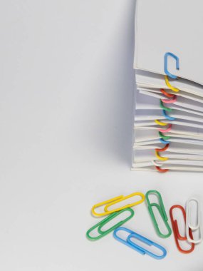 Çeşitli renkli ataçlarla tutturulmuş beyaz bir kağıt yığınının yakın plan çekimi ve aşağıda da başka ataçlar var. Görüntü, temiz beyaz bir arkaplan üzerine kurulmuş, minimalist ve organize bir estetik yaratıyor. Pap 'in renkleri