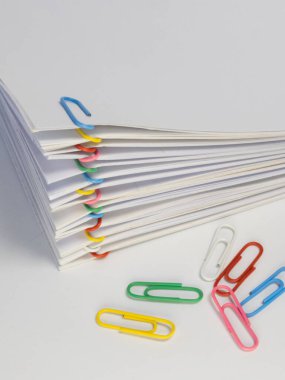 Yakın plan çekimde çeşitli renkli ataçlarla korunan bir yığın beyaz kağıt dökümanı tasvir ediliyor. Farklı renklerde birkaç ataç yığının etrafına saçıldı. Resim beyaz kağıt ve vibran arasındaki kontrastı vurgular