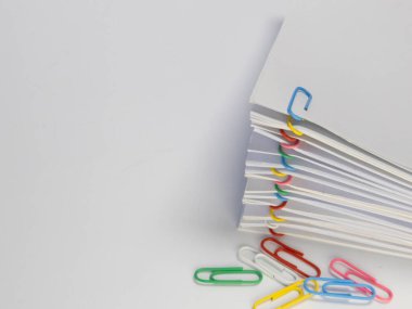 Yakın plan çekimde renkli ataçlarla tutturulmuş beyaz bir kağıt yığını yer alır. Kağıt ataçları çeşitli renklerde ve bazıları parlak beyaz bir yüzey üzerine yığının tabanına saçılmış. Kompozisyon basitliği ve orgayı vurguluyor.