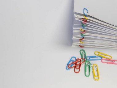 Çeşitli renkli ataçlarla tutturulmuş beyaz kağıt yığınının yakın plan çekimi. Birkaç gevşek ataç yığının yanındaki düz beyaz bir yüzeye saçılmış. Görüntü parlak, parlak beyaz kağıt ve canlı renkleri vurguluyor. 