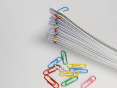 Çeşitli renkli ataçlarla tutturulmuş beyaz kağıtların yakın plan çekimi. Beyaz bir yüzeye, kağıtların etrafına bir kaç tane gevşek ataç saçılmış. Görüntü, iş veya organizasyon için uygun temiz ve düzenli bir görünüme sahip