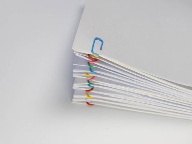 Yakın plan çekimde renkli ataçlarla bir araya getirilmiş bir yığın beyaz kağıt sergileniyor. Kağıtlar düzgünce düzenlenmiş, bir düzen ve verimlilik duygusu yaratıyor. Beyaz arkaplan kağıdın renklerini vurgular